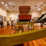 A low-angle photograph of a gallery with a replica 1800s wagon in the center of the room.