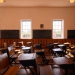 A side view of the 1885 Schoolhouse with antique desks arranged in rows.