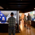 Museum visitors stand and read the labels in several exhibit cases.